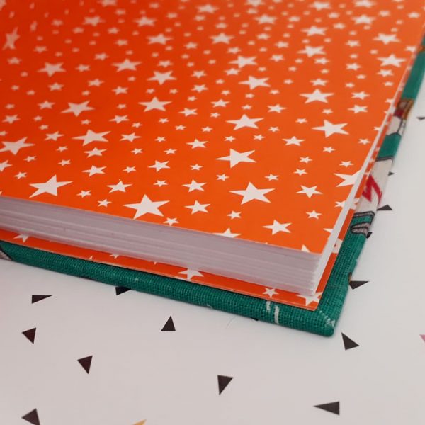 Caderno aberto, onde se vê a folha de guarda laranja com estrelas brancas.